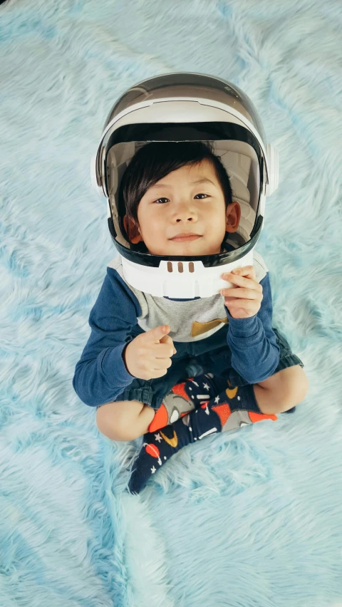 a small child in a space suit sitting on a rug, inspired by Knox Martin, pexels contest winner, wearing kneesocks, gemma chen, short light grey whiskers, smiling down from above