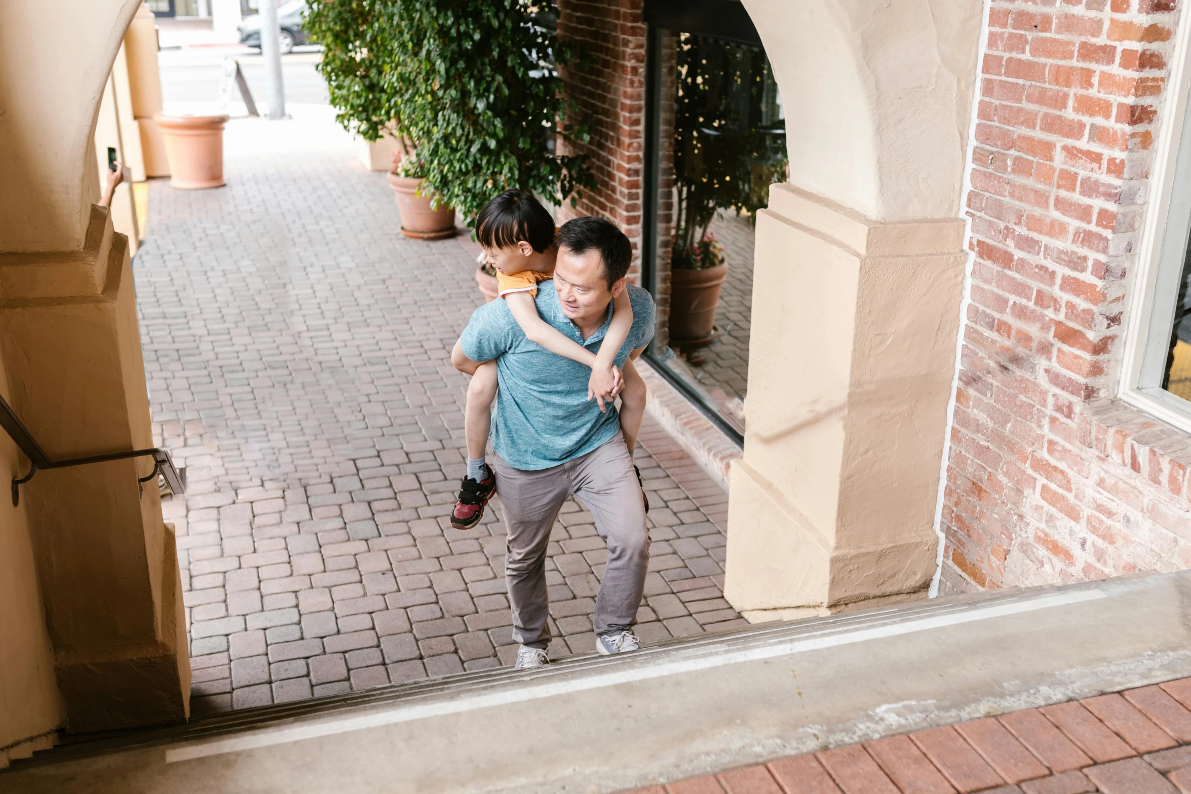 a man carrying a little girl on his back, unsplash, happening, exiting store, lee griggs and jason chan, about to enter doorframe, al fresco