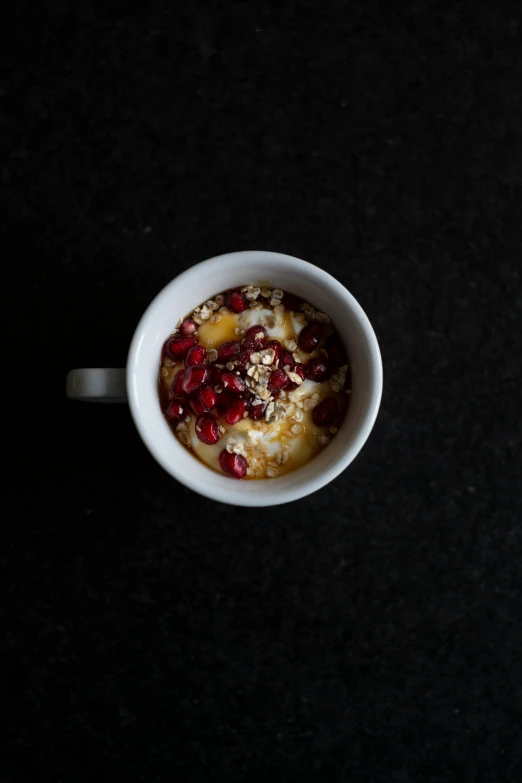 a bowl of oatmeal sitting on top of a table, in front of a black background, with a white mug, pomegranate, thumbnail