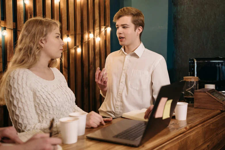 a couple of people sitting at a table with a laptop, a screenshot, trending on pexels, aussie baristas, teenage boy, standing sideways, convincing