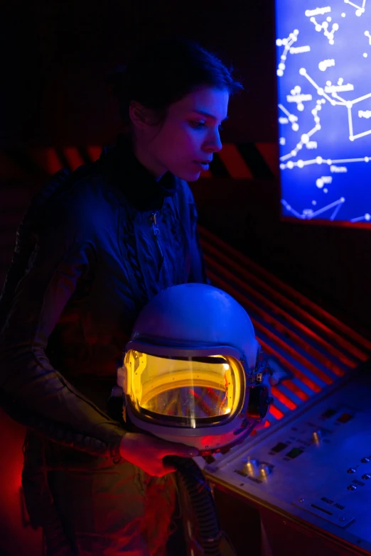 a man holding a helmet in front of a computer, inspired by roger deakins, interactive art, girl in space, luminous cockpit, wax figure, still from a wes anderson movie