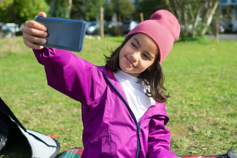 a little girl sitting on a blanket taking a selfie, wearing a purple breton cap, campsites, wearing a purple detailed coat, avatar image