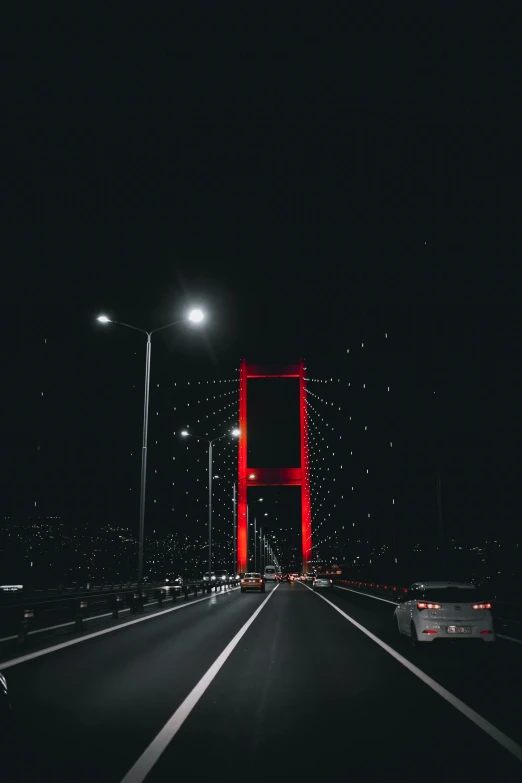 a car driving across a bridge at night, an album cover, by Ismail Acar, pexels contest winner, istanbul, red on black, snapchat photo, grey skies