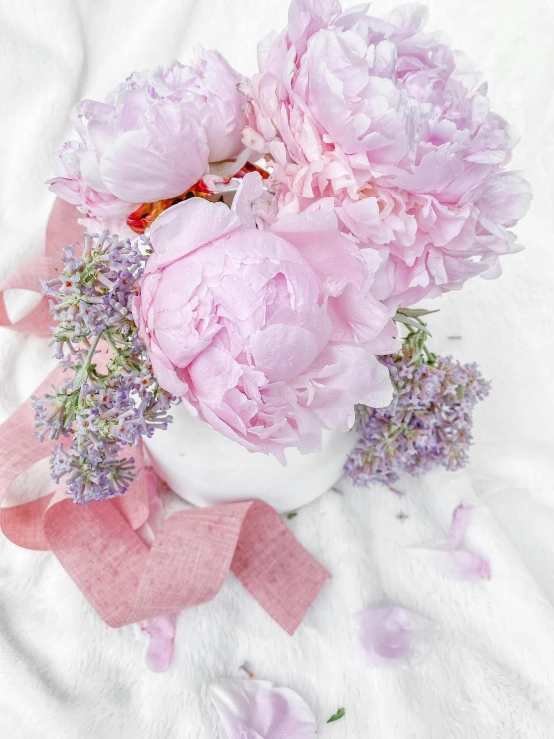 a bouquet of pink flowers sitting on top of a bed, by Lucia Peka, pexels contest winner, 🎀 🗡 🍓 🧚, lavender flowers, peony, soft white glow