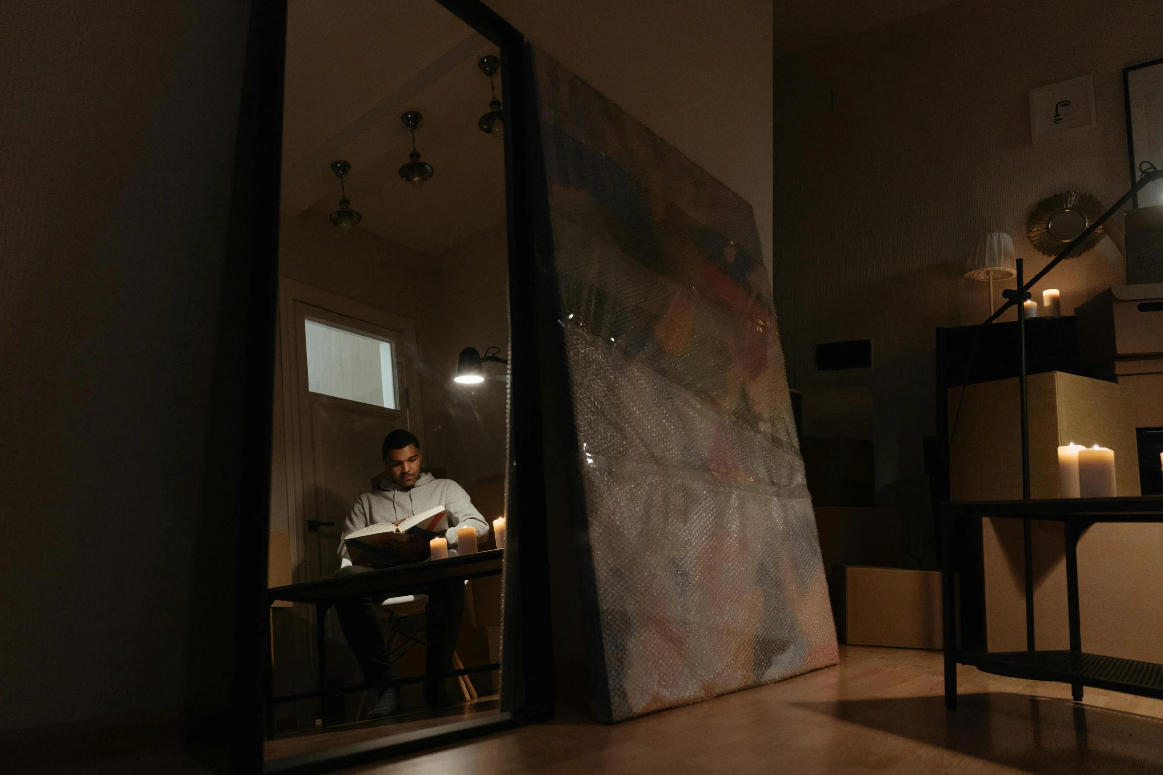 a man sitting at a table in front of a mirror, a hyperrealistic painting, pexels contest winner, low light room, art workstation, he is holding a large book, space seen outside from a window