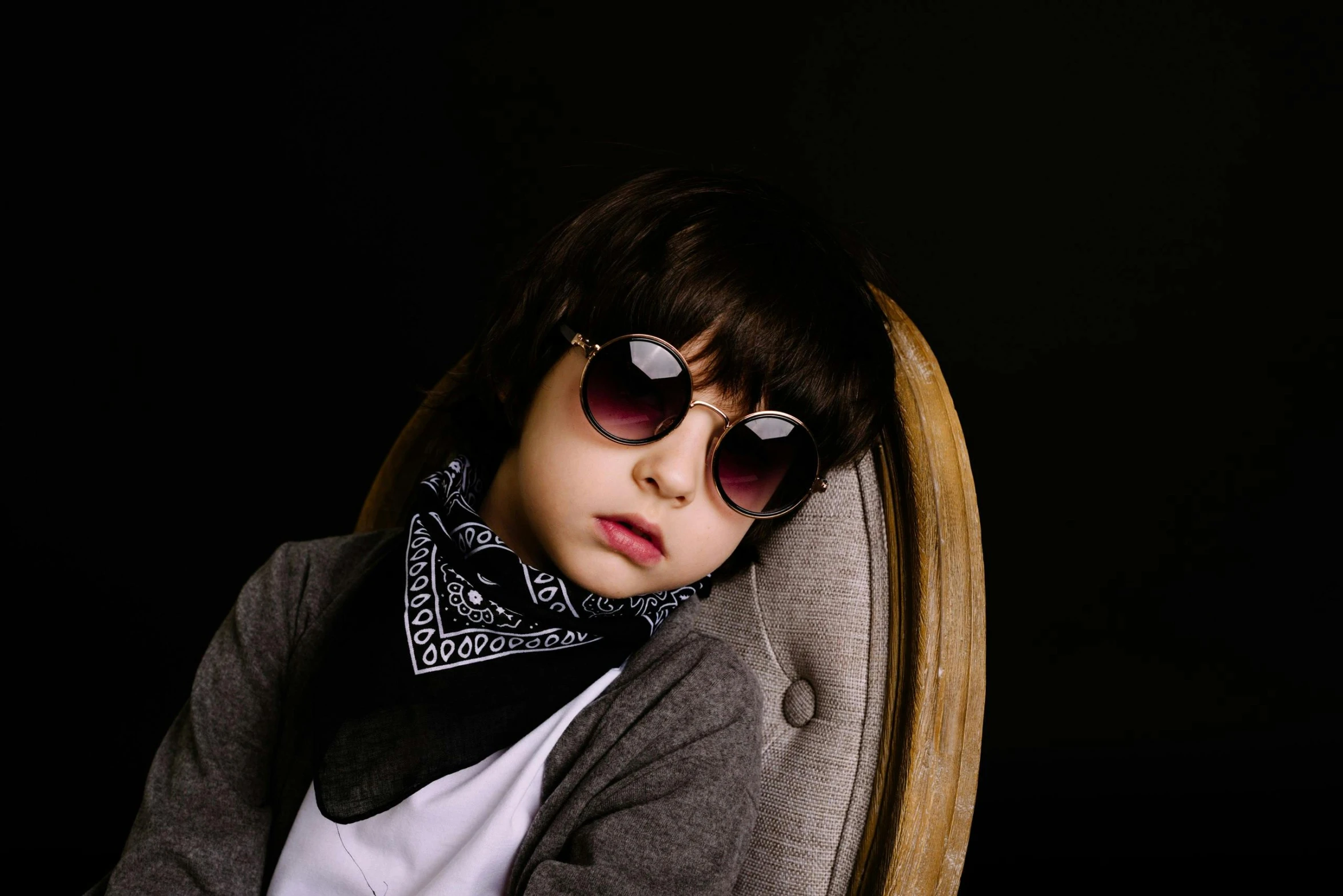 a young boy wearing sunglasses sitting in a chair, an album cover, by Nina Hamnett, trending on pexels, paisley, fashion shoot 8k, serious face, high quality photo