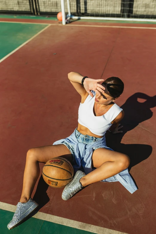 a woman sitting on a basketball court holding a basketball, trending on pexels, croptop and shorts, head tilted downward, overhead sun, sports illustrated