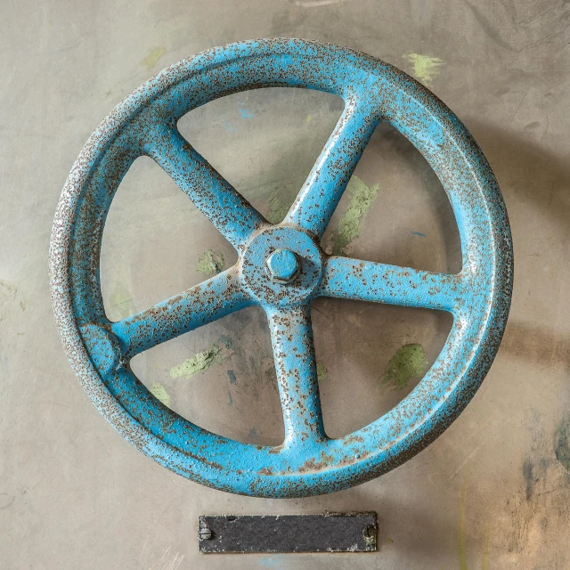 a blue fire hydrant sitting on top of a cement floor, an abstract sculpture, by Kazimierz Wojniakowski, kinetic art, single steering wheel, vintage - w 1 0 2 4, large, industrial