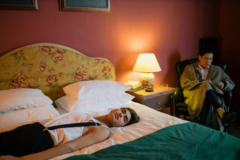 a woman laying on top of a bed next to a lamp, inspired by Nan Goldin, pexels contest winner, happening, wes anderson and wes anderson, medium shot of two characters, paris hotel style, teenage boy