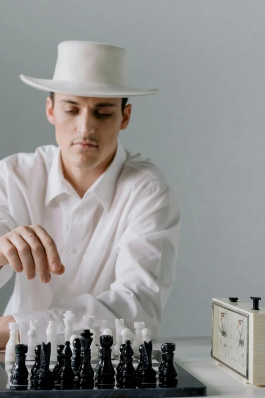 a man in a hat playing a game of chess, an album cover, inspired by Harry Haenigsen, unsplash, synthetism, dressed in white, young spanish man, dna experiment, ignant