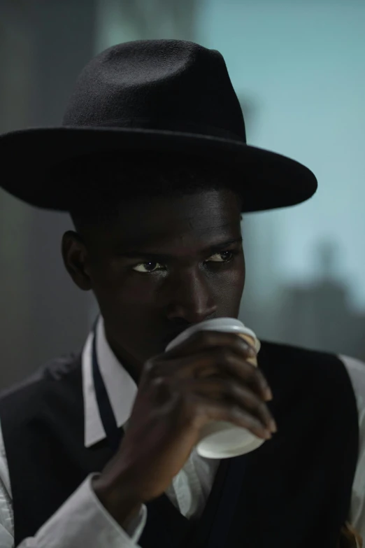 a man in a hat drinking from a cup, inspired by Gordon Parks, magical realism, adut akech, filmstill, gal yosef, religious