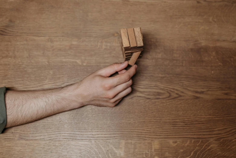 a person holding clothes pegs on a wooden floor, by Matthias Stom, unsplash, kinetic art, square masculine jaw, tower of babel, wood burn, walnut wood