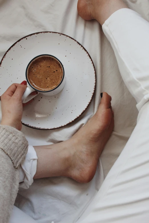 a person laying in bed with a cup of coffee, by Lucia Peka, barefeet, beige, cold brew coffee ), milk and mocha style