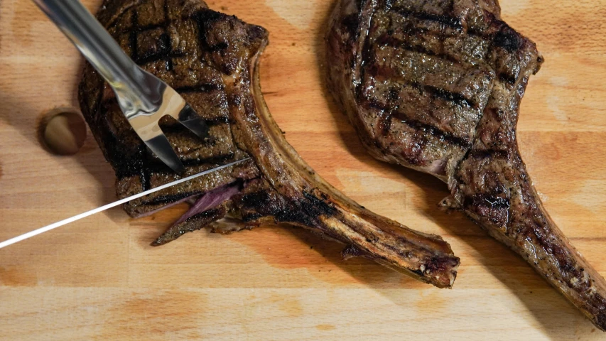 a couple of steaks sitting on top of a wooden cutting board, fork, image