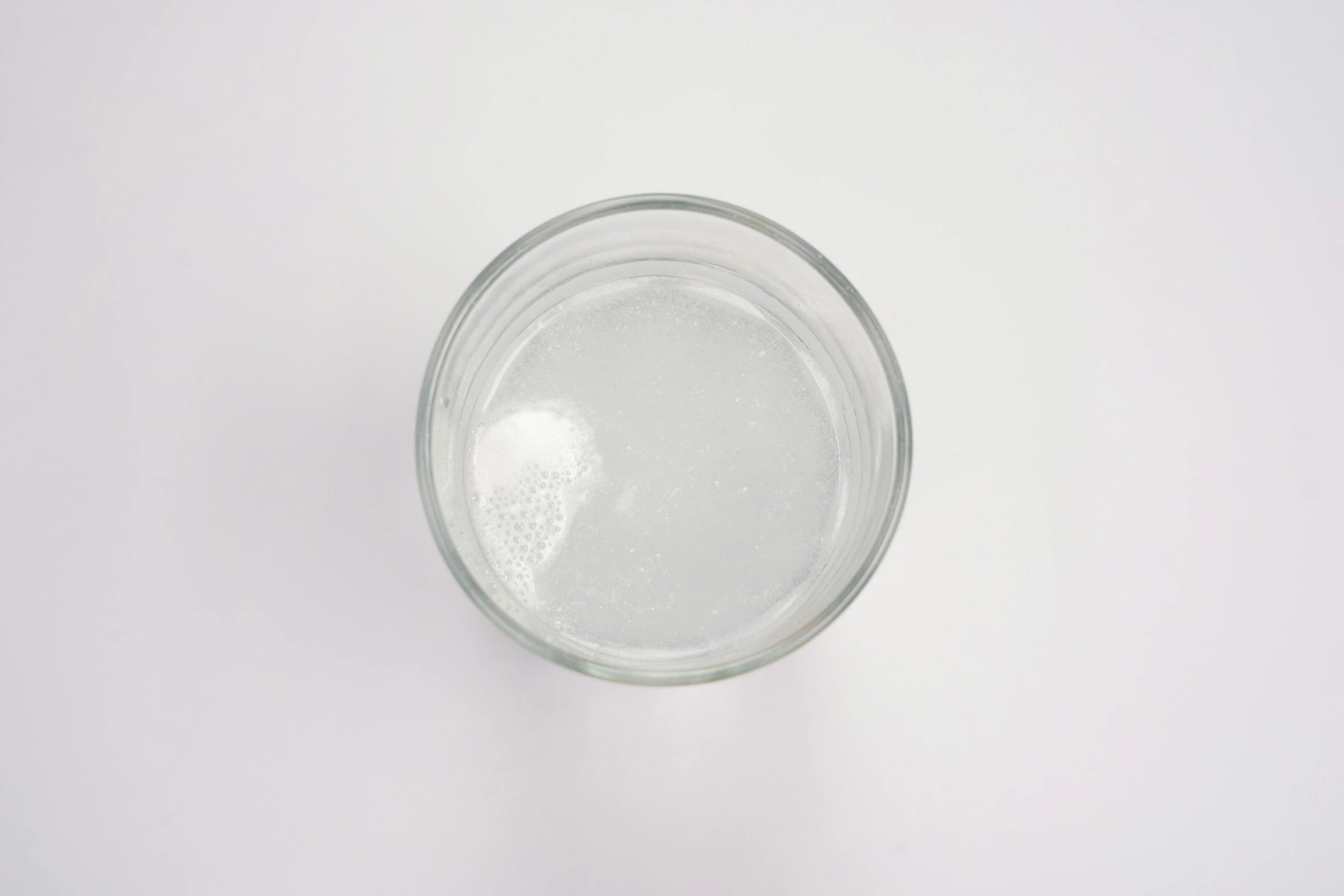 a glass of water sitting on top of a table, top down view, white sky, gelatine silver process, round bottle