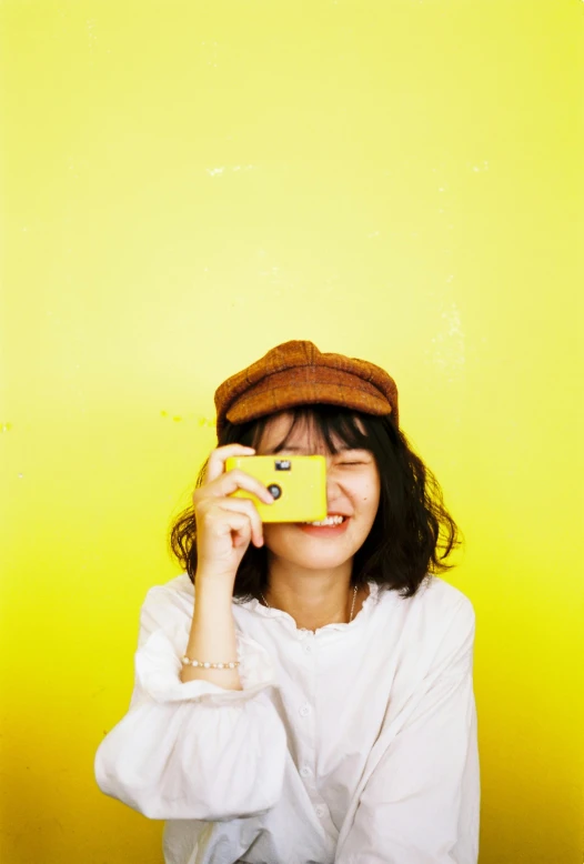 a woman taking a picture with a yellow camera, by Maeda Masao, pexels contest winner, photo booth, wearing a cute hat, single color, cute:2