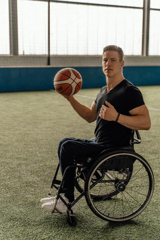 a man in a wheel chair holding a basketball, by Adam Marczyński, dribble contest winner, soccer players martin ødegaard, profile image, portrait of tall, model is wearing techtical vest