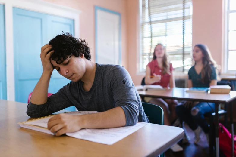 a young man sitting at a desk in a classroom, by Julian Allen, stressing out, background image, lachlan bailey, lynn skordal