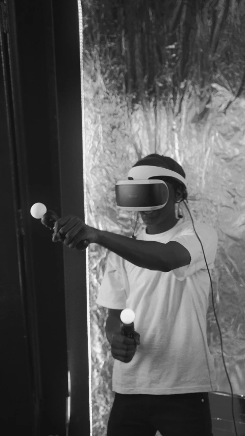 a black and white photo of a person holding a nintendo wii controller, afrofuturism, using a vr headset, virtual installation, gunfire, 2000s photo