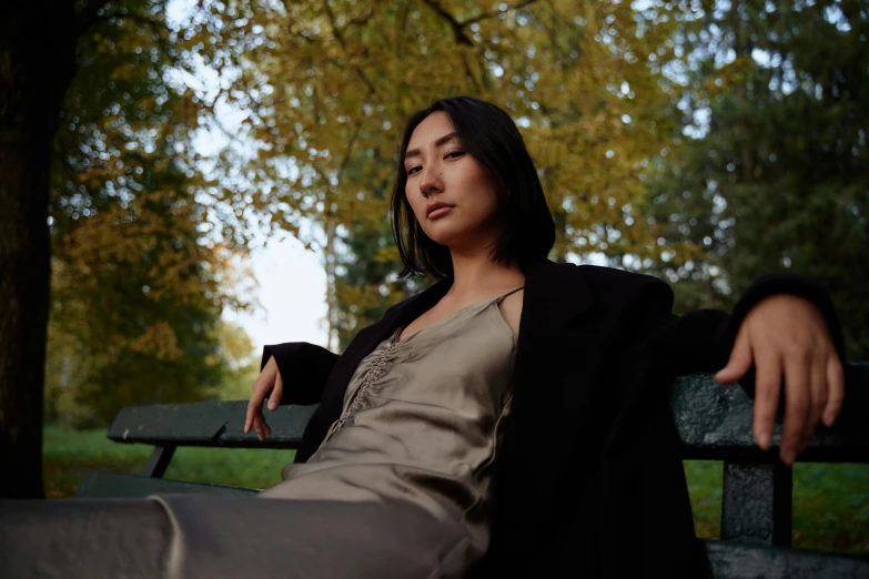 a woman sitting on a bench in a park, an album cover, inspired by Jung Park, pexels contest winner, wearing black silk robe, asian descent, wearing a leather trench coat, medium format. soft light