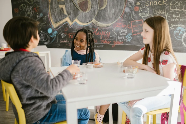 three girls sitting at a table in front of a chalkboard, by Anna Findlay, pexels contest winner, on a white table, any racial background, group sit at table, thumbnail