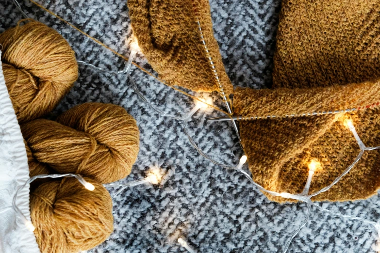 a pair of mittens sitting on top of a blanket, by Julia Pishtar, trending on pexels, arts and crafts movement, string lights, ocher, yarn ball, brown