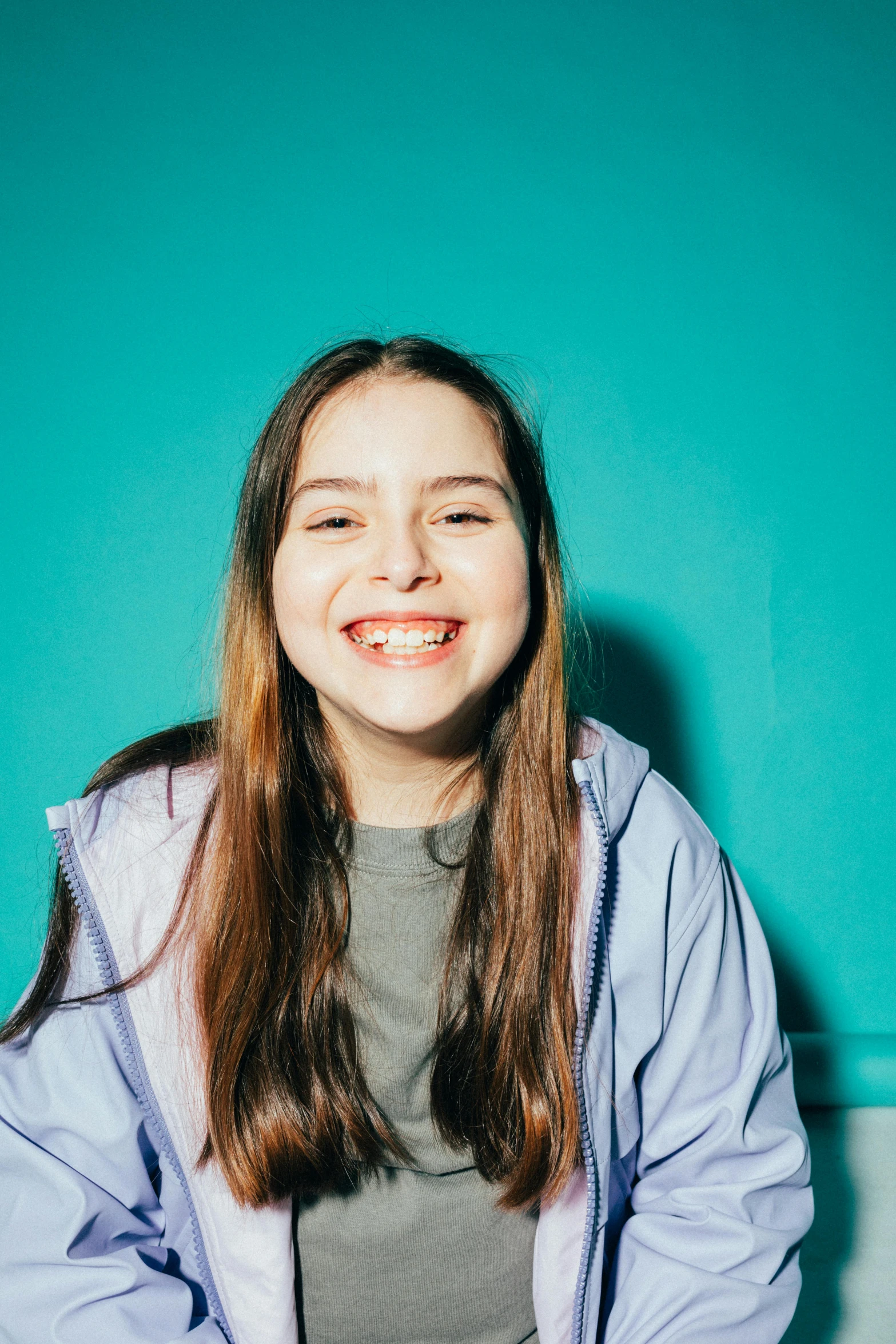 a girl sitting on a bench in front of a blue wall, an album cover, by Grace Polit, pexels contest winner, incoherents, greta thunberg smiling, extra teeth, girl in studio, wearing a blue hoodie