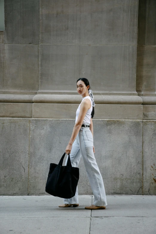 a woman walking down a sidewalk carrying a black bag, pexels contest winner, renaissance, wearing overalls, off - white collection, rodin style, she is wearing a black tank top