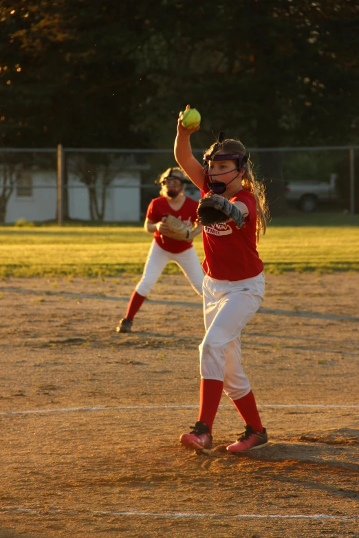 a young girl pitching a baseball on top of a field, flickr, evening time, reds, 15081959 21121991 01012000 4k, action sports