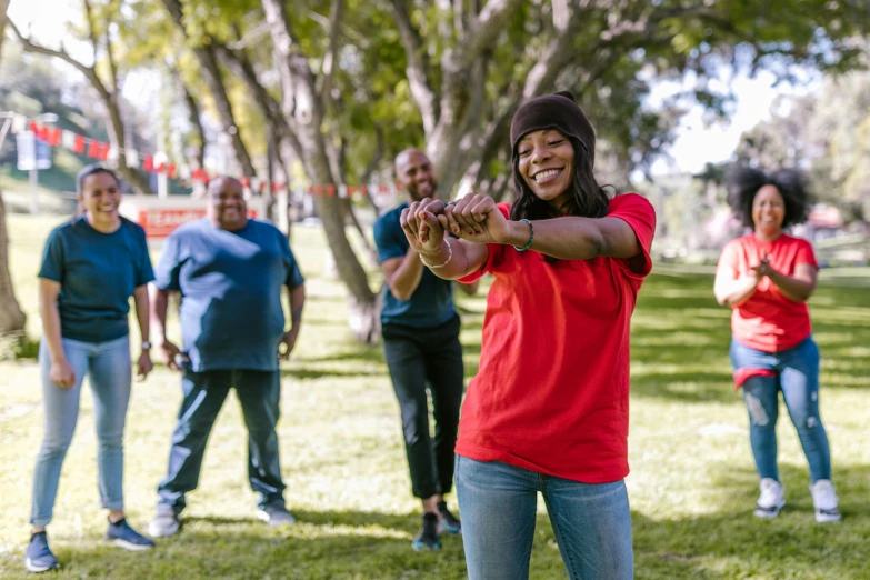 a group of people standing on top of a lush green field, red sport clothing, at a park, tai chi, photo of a black woman
