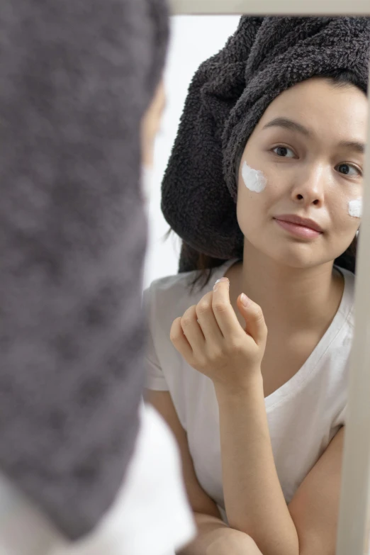 a woman putting cream on her face in front of a mirror, trending on pexels, renaissance, south east asian with round face, profile pic, grey, banner