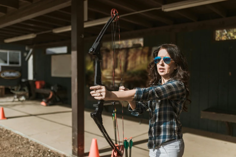 a woman in plaid shirt holding a bow and arrow, sports setting, 🕹️ 😎 🔫 🤖 🚬, instagram post, recreation