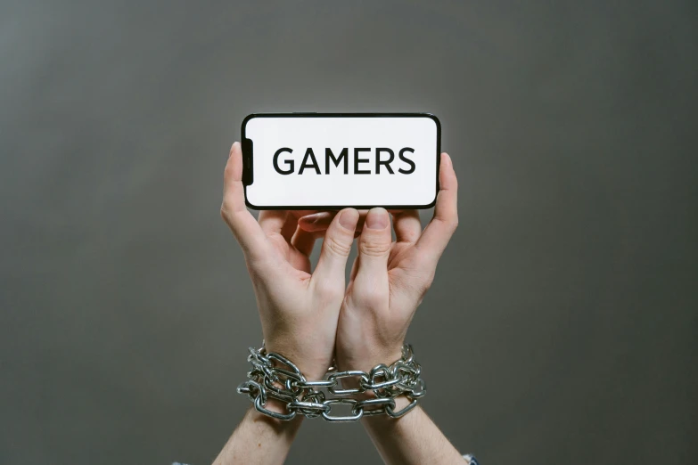 a person holding up a phone with the word gamers on it, by Julia Pishtar, ((chains)), criminals, gaming pc, 1x