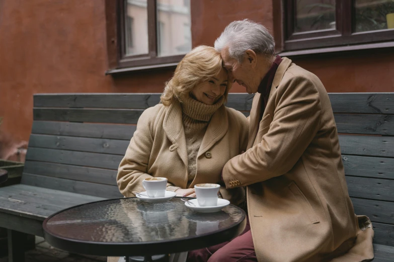 a man and a woman sitting at a table, by Jesper Knudsen, pexels contest winner, mature, brown, coffee cups, embracing