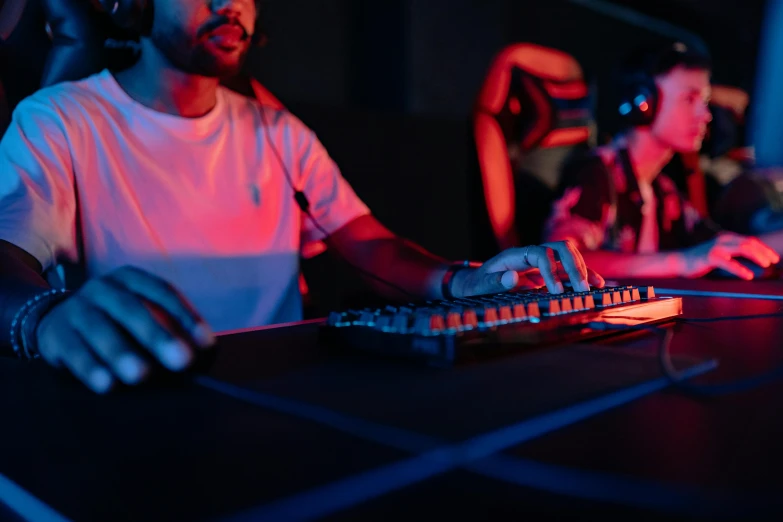 a man sitting at a table in front of a keyboard, red and blue black light, controller deck, background image, penguinz0