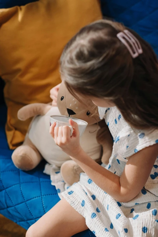 a little girl sitting on a couch with a teddy bear, by Julia Pishtar, drinking cough syrup, blue'snappy gifts'plush doll, close up shot from the side, children playing with pogs