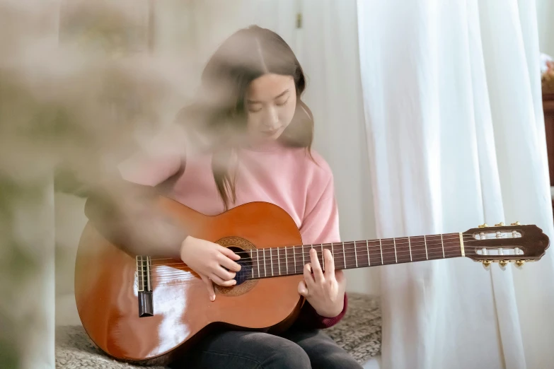 a woman sitting on a couch playing a guitar, inspired by William Stott, pexels contest winner, young asian girl, background image, performance, slight overcast