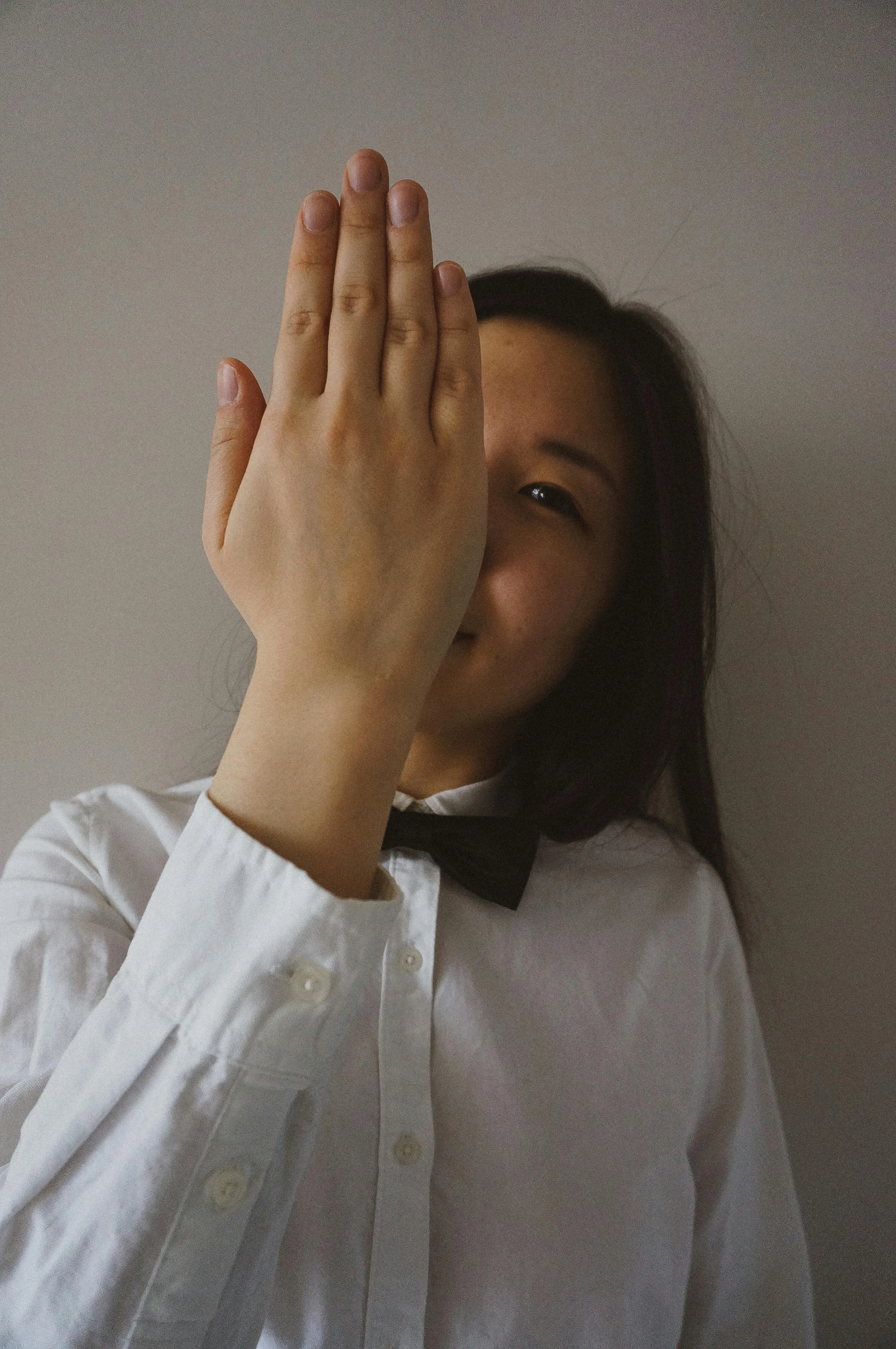 a woman holding her hands up in front of her face, unsplash, renaissance, wearing a shirt with a tie, wearing a white tuxedo, asian women, bow tie