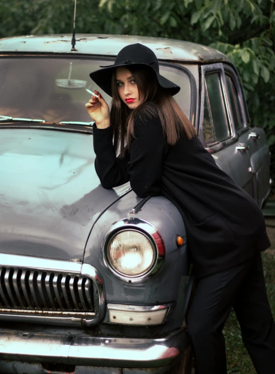 a woman leaning on the hood of an old car, inspired by Elsa Bleda, pexels contest winner, wearing black old dress and hat, girl in suit, instagram post, lipstick
