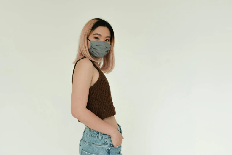 a woman wearing a face mask in front of a white background, a picture, trending on pexels, aestheticism, croptop, gray, green and brown clothes, asian human