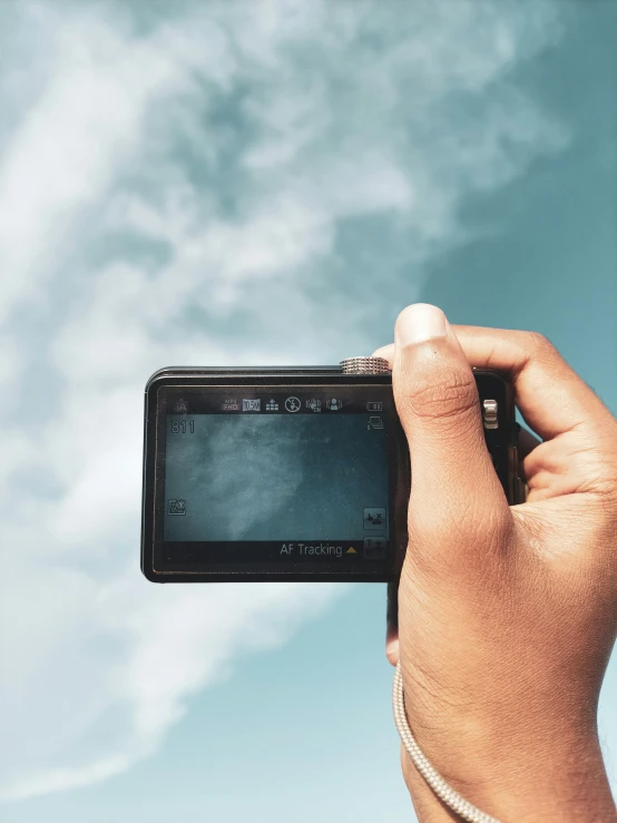 a person taking a picture with a camera, with clouds in the sky, lcd screen, pointing at the camera, grainy photograph