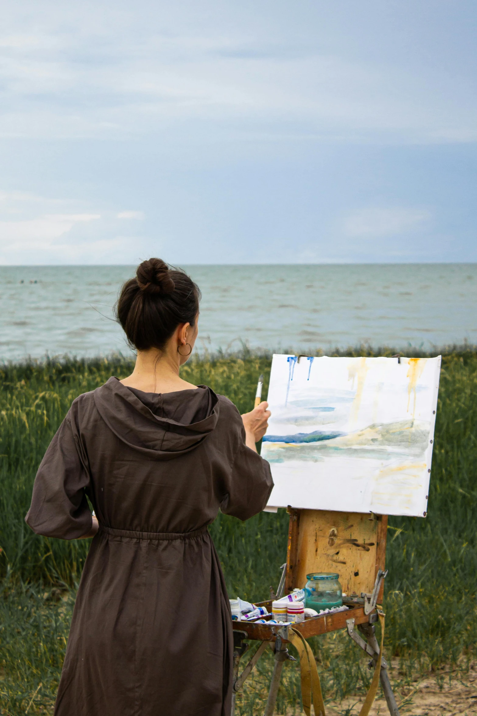 a woman that is standing in front of a painting, inspired by Wilhelm Hammershøi, pexels contest winner, plein air, seaview, expressive brushstrokes, easel, grey