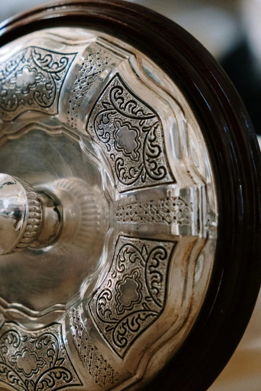 a silver plate sitting on top of a wooden table, arabesque, hoog detail, preserved museum piece, upclose, gong