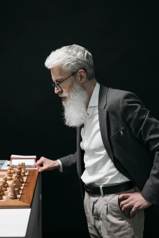 a man standing in front of a chess board, white long beard, ai researcher, right hand side profile, man with glasses
