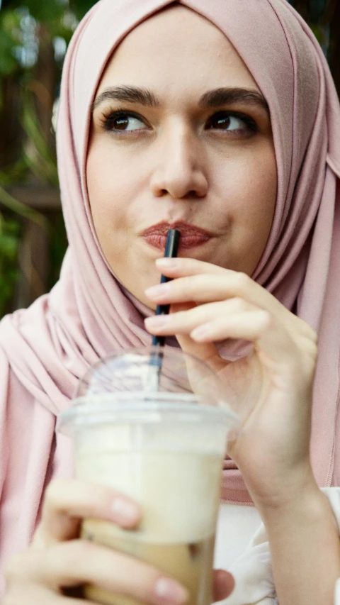 a woman wearing a hijab drinking a drink, by Adam Marczyński, shutterstock, drink milkshakes together, square, 15081959 21121991 01012000 4k, closeup at the food