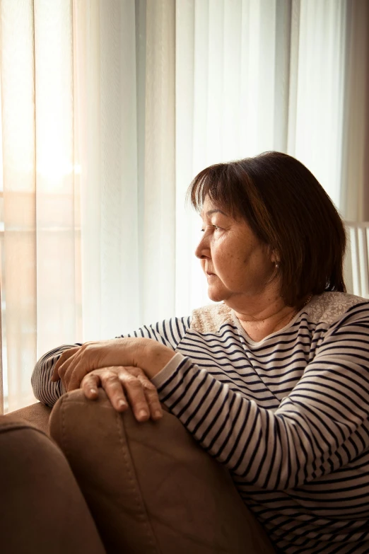 a woman sitting on a couch looking out a window, a portrait, shutterstock, grieving, high resolution photo, aged, multiple stories