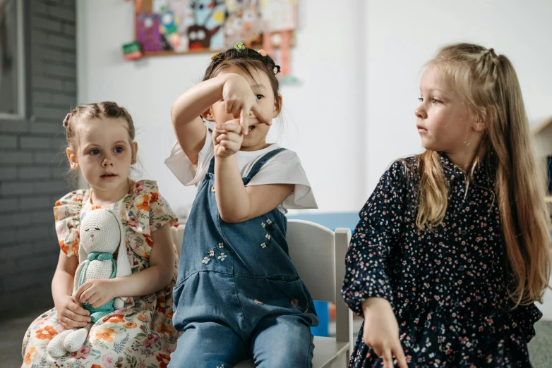 a group of little girls sitting next to each other, by Emma Andijewska, pexels contest winner, process art, shrugging arms, 15081959 21121991 01012000 4k, playing games, three fourths view