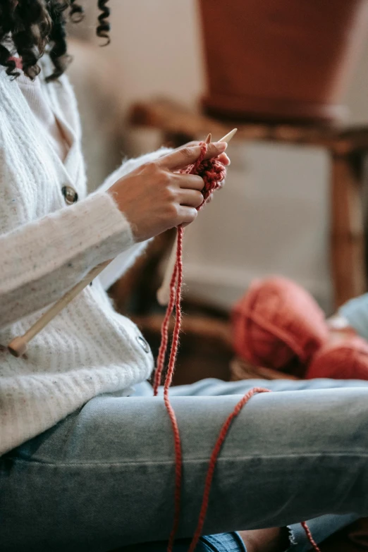 a woman sitting on the floor knitting a ball of yarn, trending on pexels, arts and crafts movement, red sweater and gray pants, made of beads and yarn, spinning, red fabric