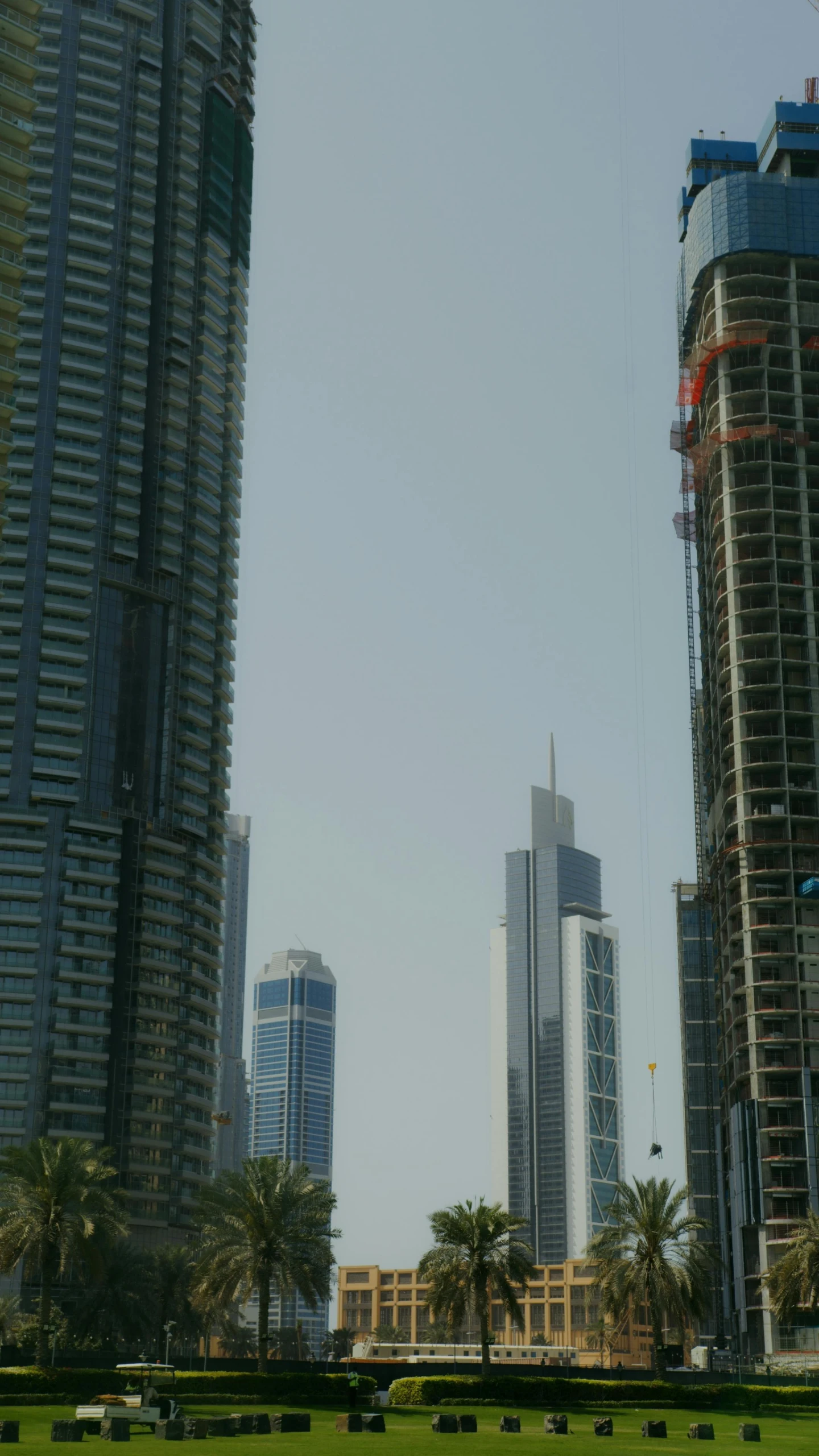 a man flying a kite on top of a lush green field, an album cover, inspired by Zaha Hadid, pexels, hurufiyya, with tall glass skyscrapers, sheikh mohammed ruler of dubai, view from across the street, sparse detail