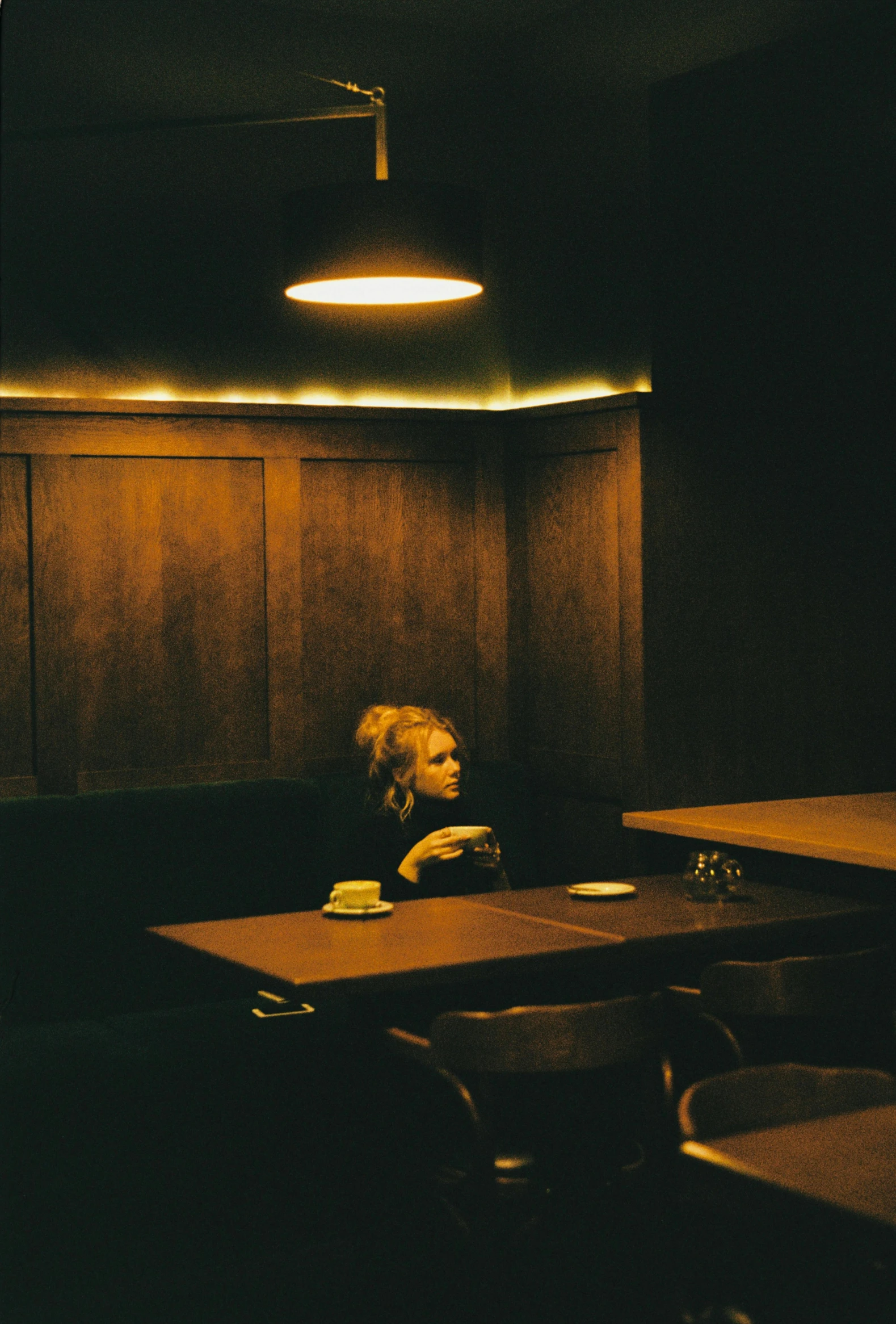 a person sitting at a table in a dark room, an album cover, inspired by Elsa Bleda, unsplash, tonalism, diner caffee, a blond, 3 5 mm kodak color ektochrome, pensive lonely